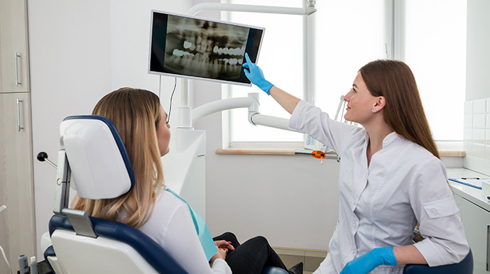 Dentist pointing to a panoramic x-ray image on a computer monitor for her patient
