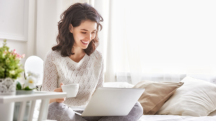 Smiling woman holding coffee cup and looking at a computer laptop