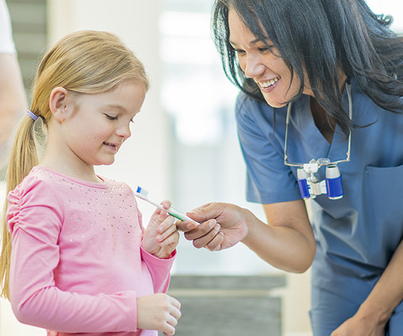 Dental hygienist handing a girl a toothbrush